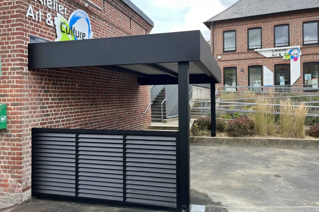 Abri Moduleo type abribus en aluminium noir avec clôture Sarlande, adossé à un bâtiment municipal