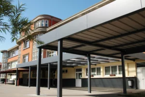 Abri - Préau d'école en aluminium sur mesure modèle MODULEO EUROFACTORY, adossé à l'établissement avec toiture en bac acier et polycarbonate, fabrication française