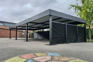 Abri - Préau autoporté rectangulaire MODULEO en aluminium sur-mesure, avec brise-vue SARLANDE noir sur deux longueurs pour protéger du vent et de la pluie, installé dans la cour d’école