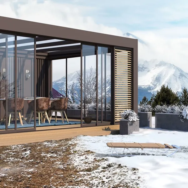 Pergola LINEA autoportée en aluminium sur mesure marron avec panneaux vitrés, située en montagne avec vue sur les sommets enneigés.